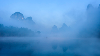 A boat glides across a misty Li River, Quilin, China