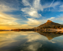 A couple dwarfed by the mountains on a rare calm Camps Bay sunset, Cape Town 