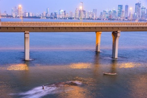 Determined Mumbai Fisherman stands in the ocean with the city lights coming on in the background